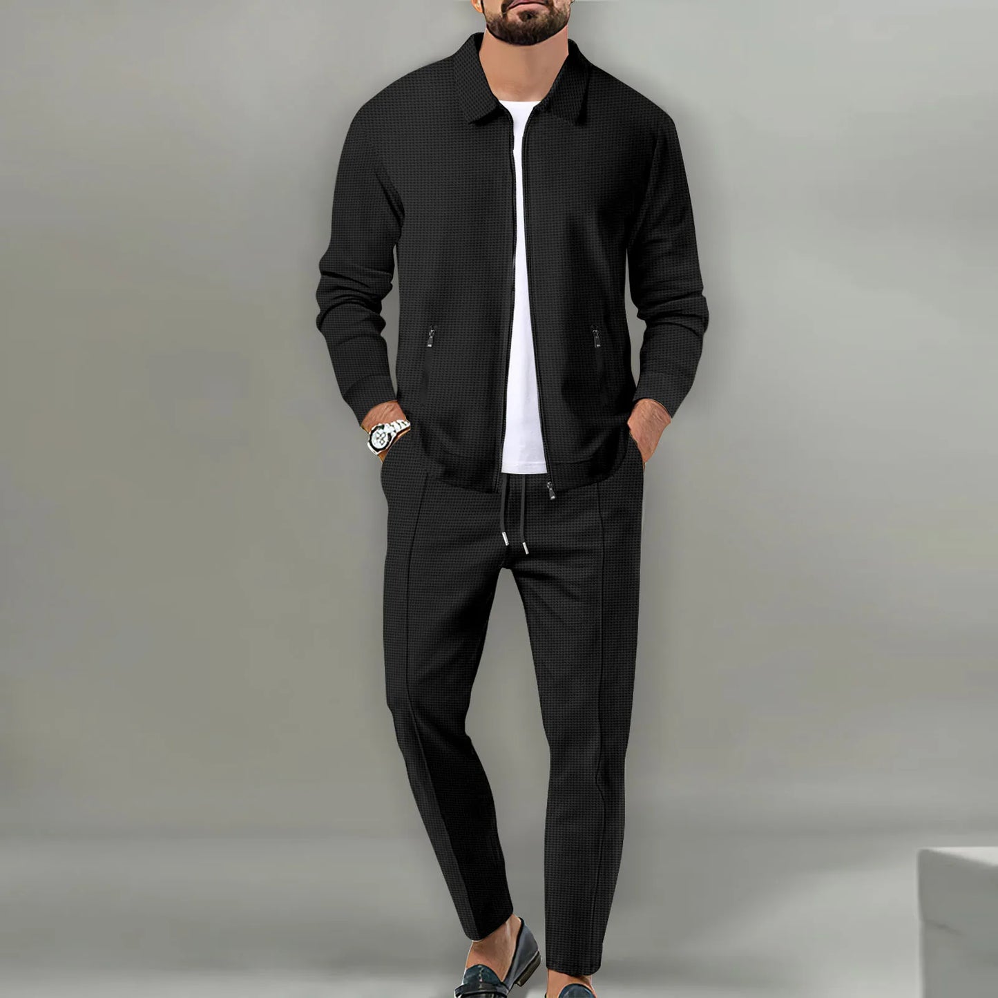 Man wearing a black jacket and pants with a white shirt against a gray background