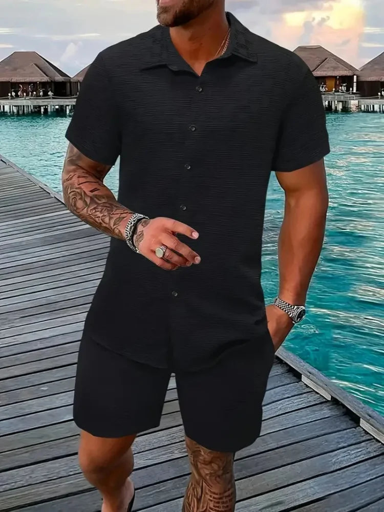 A man wearing a white short-sleeved shirt and matching shorts with a drawstring closure, standing near a poolside.