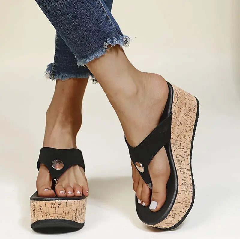 Black sandals with cork platforms worn by a person with rolled-up jeans.