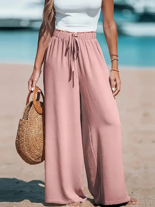 Person wearing pink wide-leg pants and a white top on a beach.