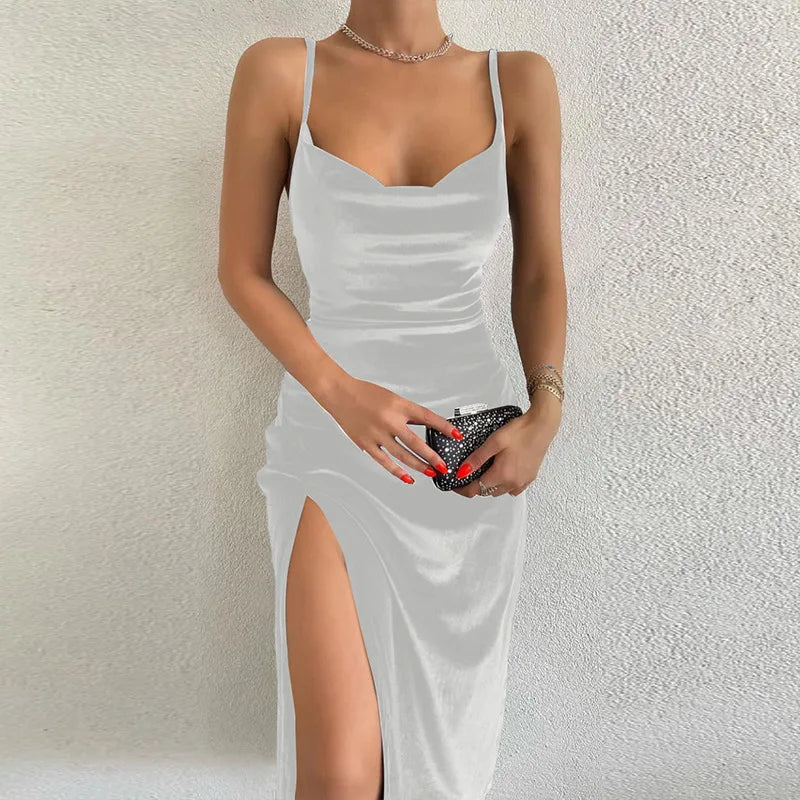 Woman wearing a white dress with a slit, holding a clutch against a textured wall.