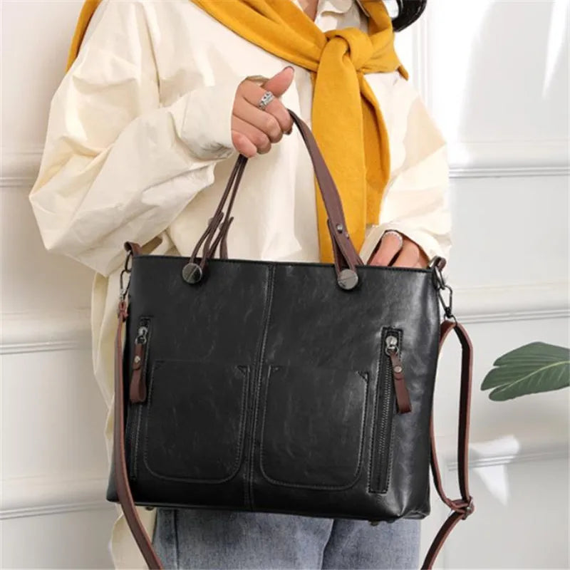 Person holding a black handbag with brown straps against a white wall.