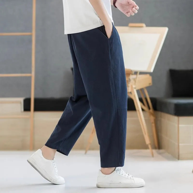 Person wearing navy blue pants and white sneakers in a minimalistic room.
