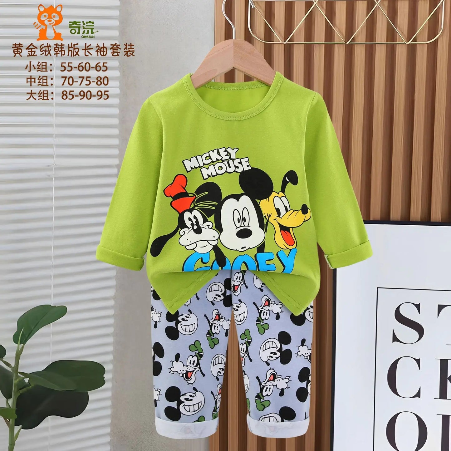 Green shirt with Mickey Mouse design and matching pants on a hanger against a wooden background.