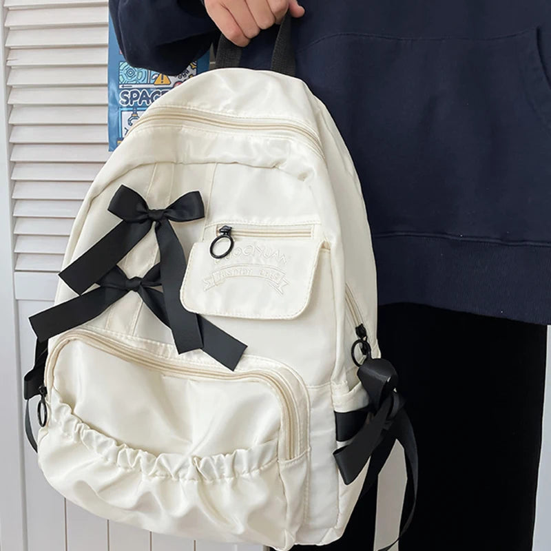 White backpack with black ribbons held by a person against a white background