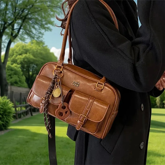 Brown leather bag with gold accents held by a person in a black coat outdoors.