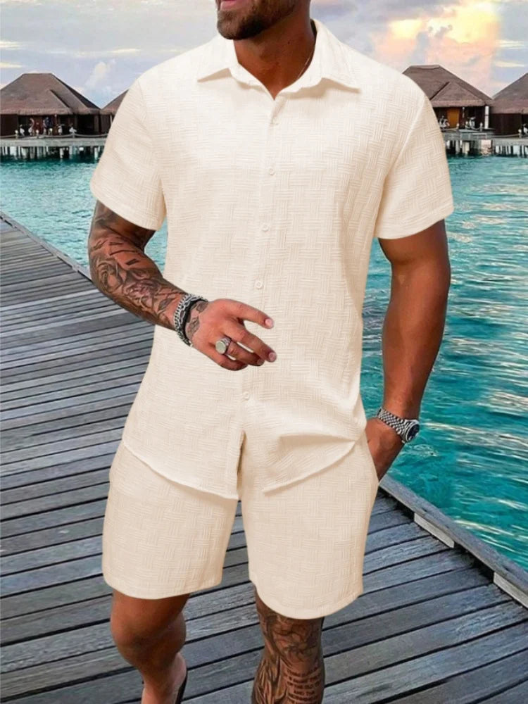 A man wearing a white short-sleeved shirt and matching shorts with a drawstring closure, standing near a poolside.