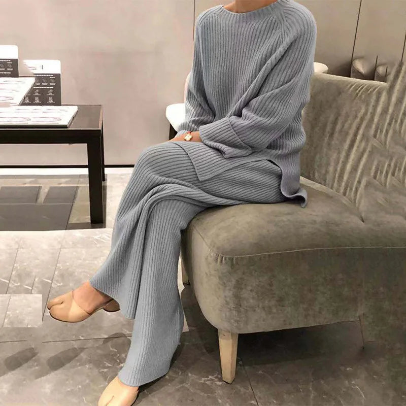 Person wearing a gray knit outfit sitting on a gray sofa in a modern room.
