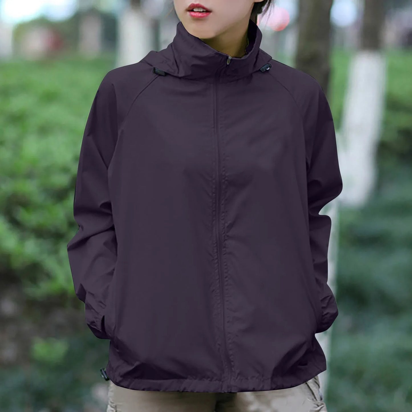 Person wearing a dark purple jacket in an outdoor setting with greenery.