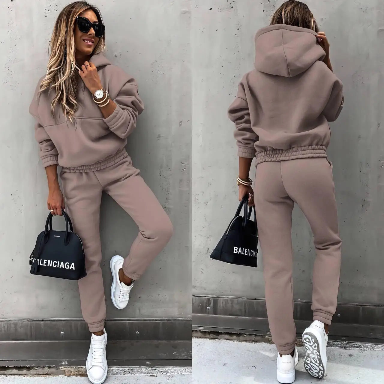 Woman wearing a brown tracksuit with Balenciaga bag against a gray wall