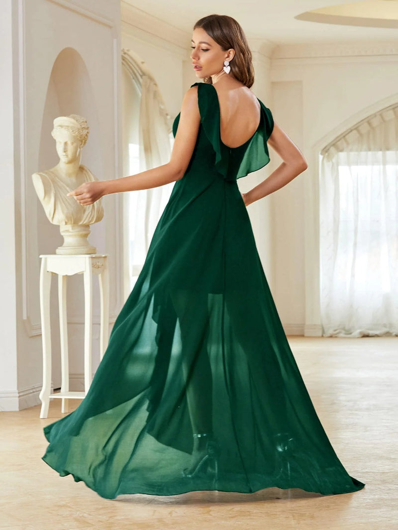 Woman in a green evening gown standing in an elegant room with classical decor.