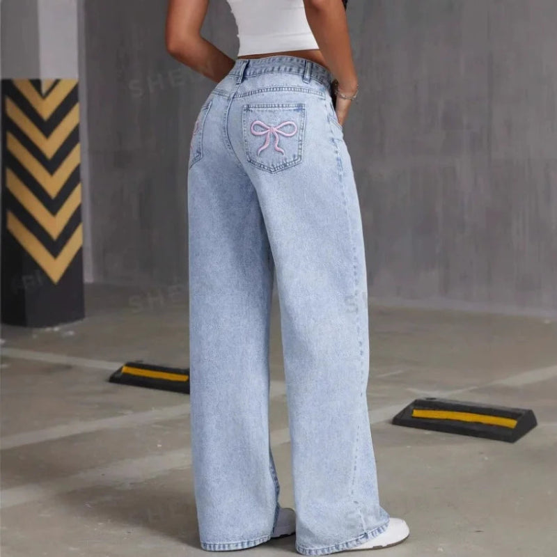 Person wearing light blue jeans with a decorative bow detail in an indoor setting.