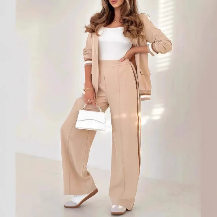 Woman wearing a beige outfit with wide-leg pants and a matching jacket, holding a white handbag.