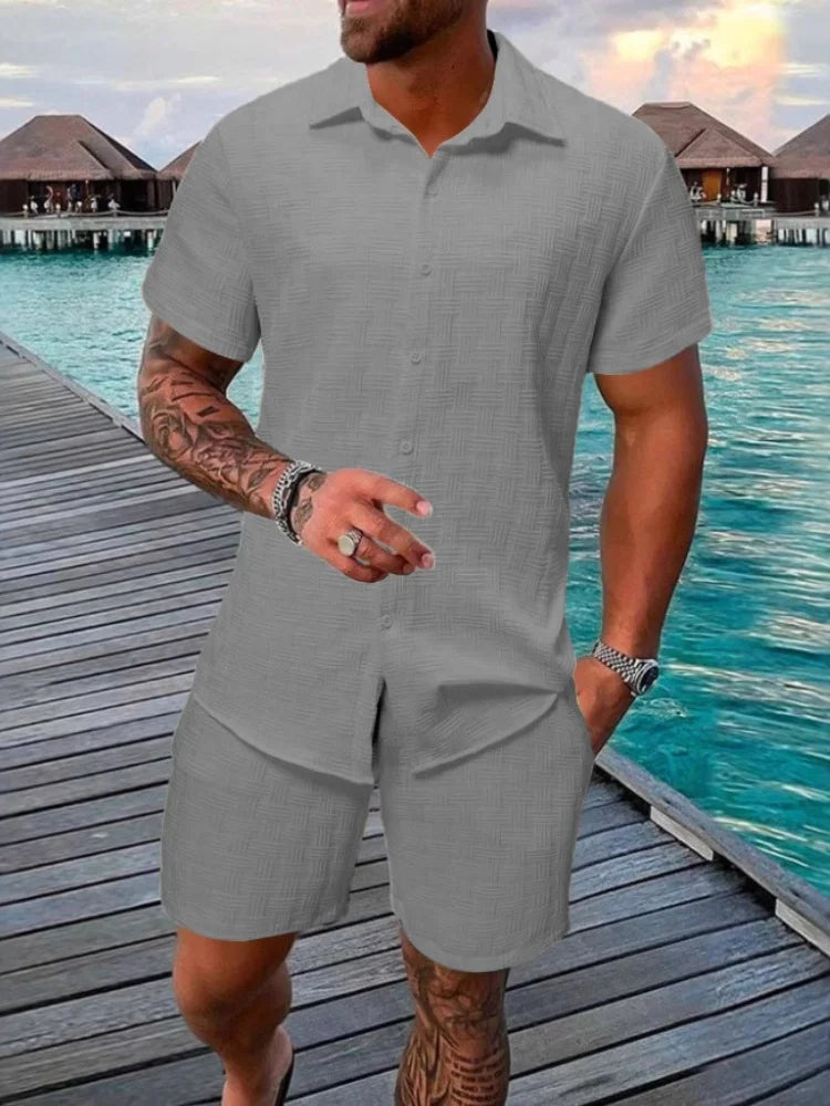 A man wearing a white short-sleeved shirt and matching shorts with a drawstring closure, standing near a poolside.