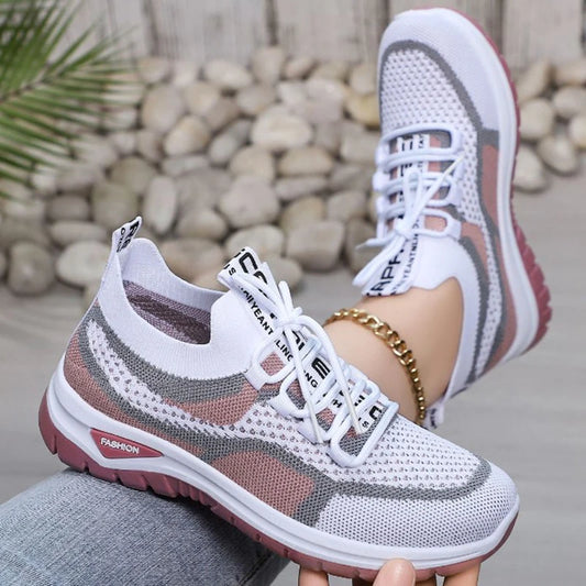 White and gray sneakers with pink soles worn by a person sitting on rocks.