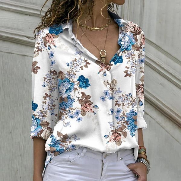 Woman wearing a white blouse with blue floral embroidery against a neutral background