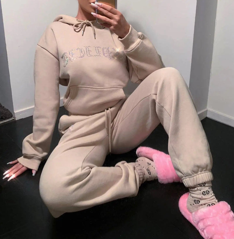 Person wearing a beige tracksuit with pink slippers sitting on a black floor.