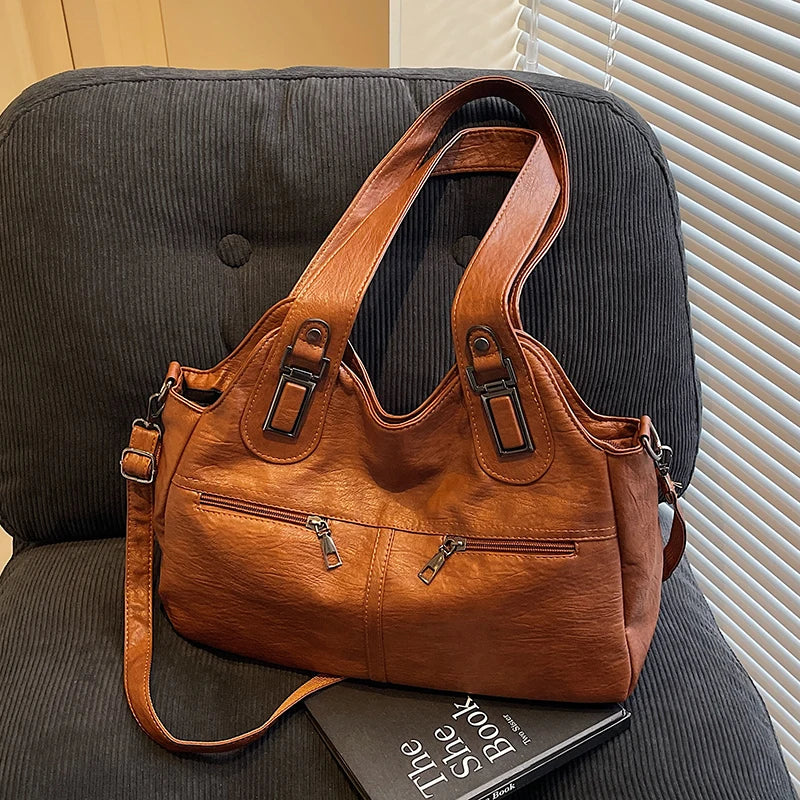 Brown leather handbag on a dark surface with a book underneath