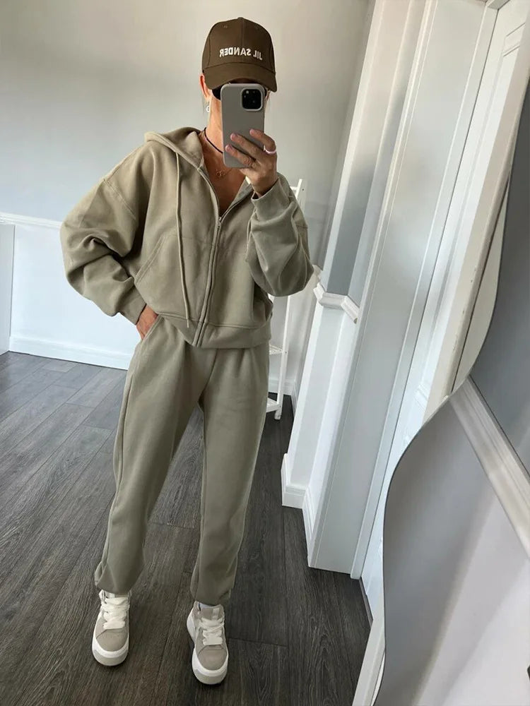 Person wearing a beige tracksuit and brown cap taking a mirror selfie.