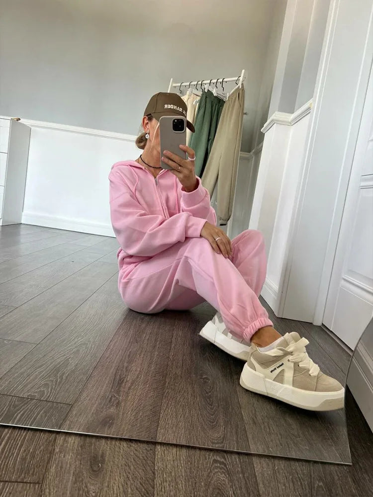 Person in pink tracksuit sitting on the floor taking a mirror selfie.