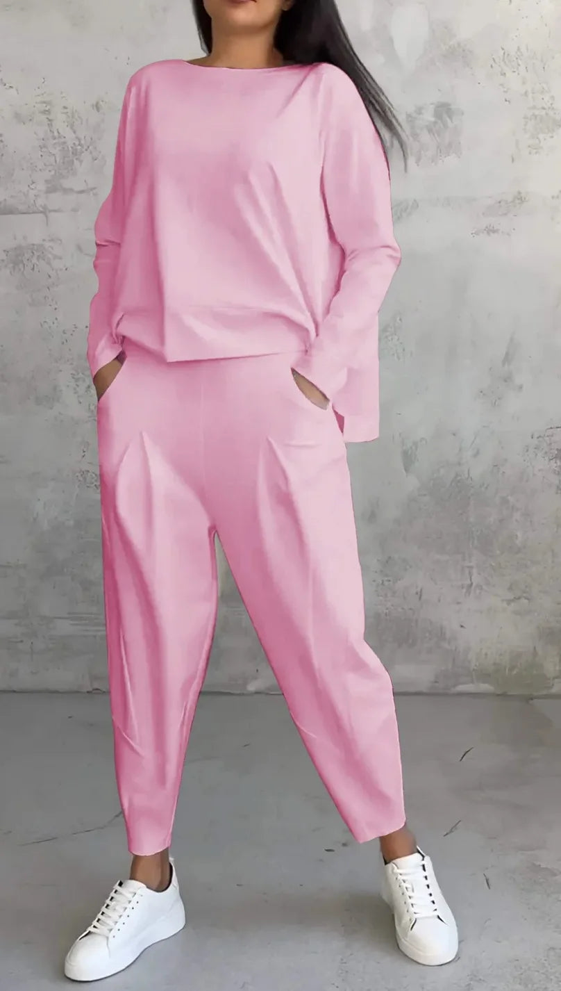 Person wearing a pink outfit with white sneakers against a gray concrete wall.
