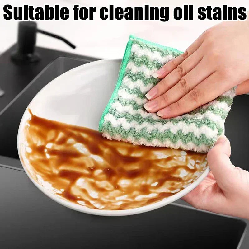 Hand using a green sponge to clean an oil-stained dish in a kitchen setting.