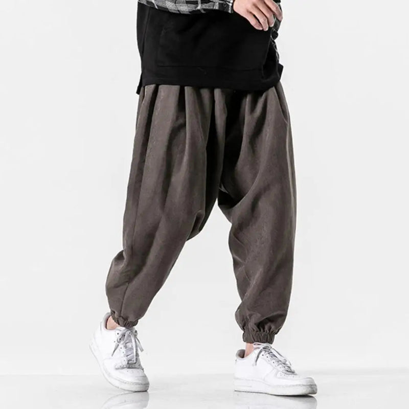 Person wearing dark brown baggy pants and white sneakers on a light gray background