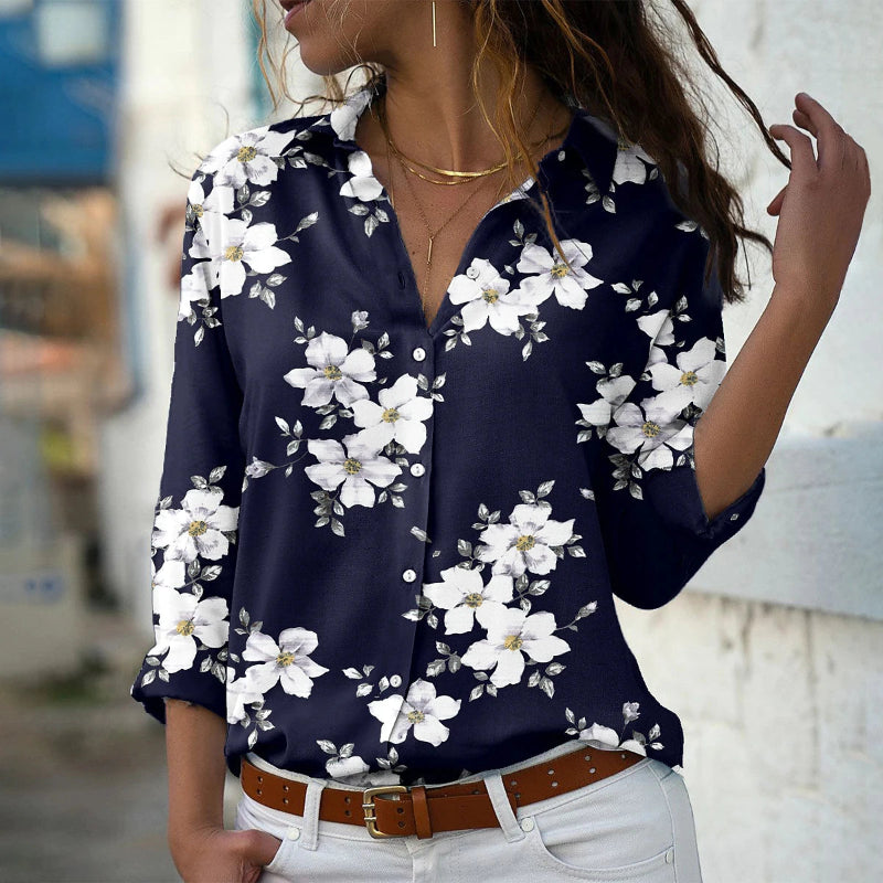 Woman wearing a navy blue floral blouse with white flowers, white pants, and a brown belt.