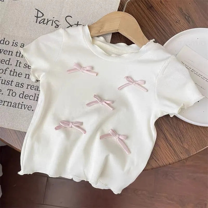 White baby dress with pink bows on a wooden surface