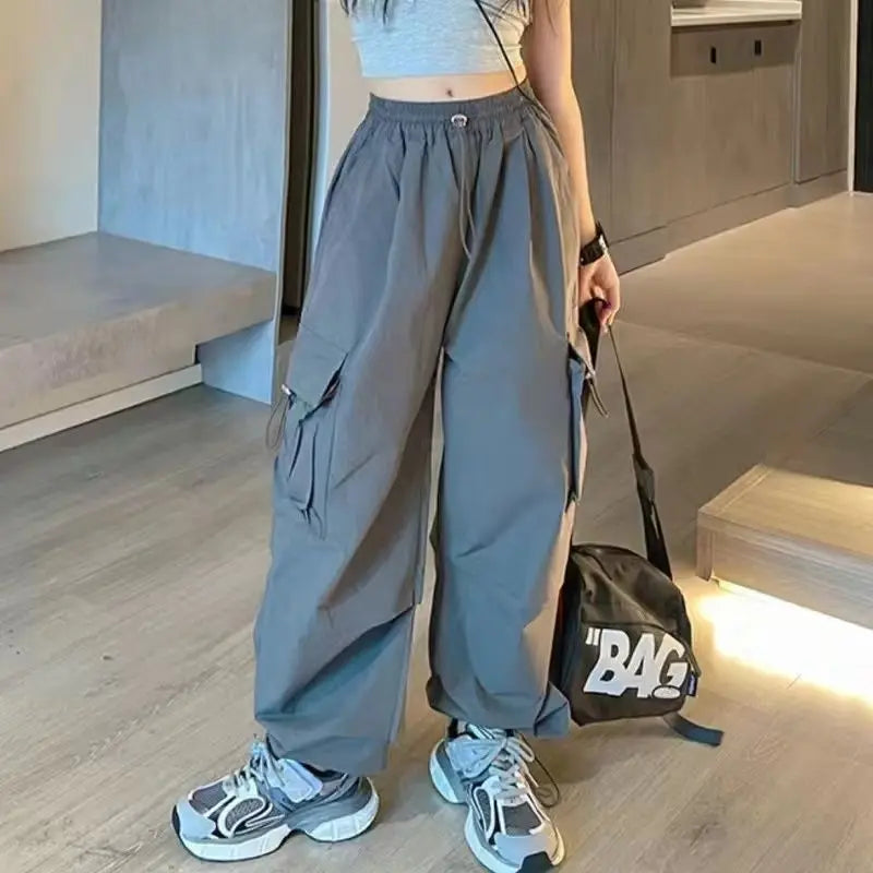Person wearing gray high-waisted pants and white sneakers, holding a black bag with 'BAG' written on it, indoors.
