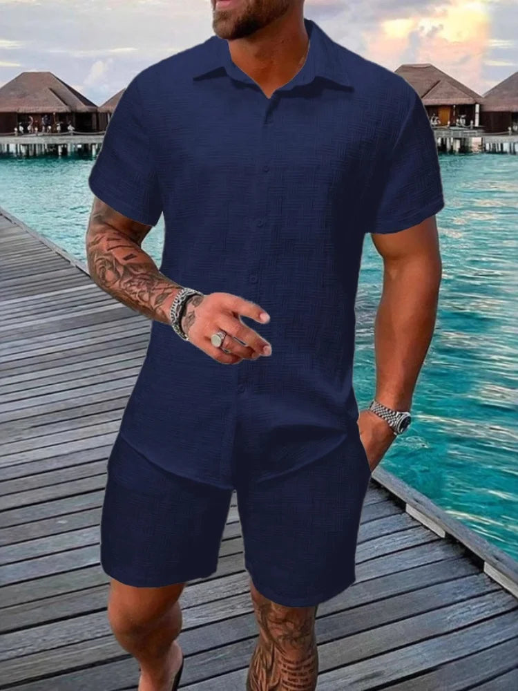 A man wearing a white short-sleeved shirt and matching shorts with a drawstring closure, standing near a poolside.