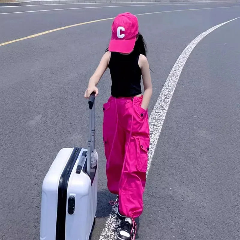 Person wearing a pink cap and pants with a white suitcase on an asphalt road.