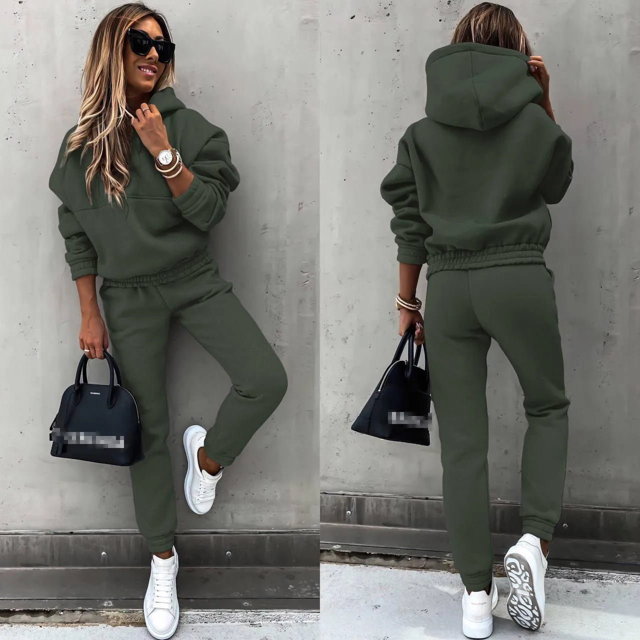 Woman wearing a green tracksuit with white sneakers, holding a black handbag against a gray wall.