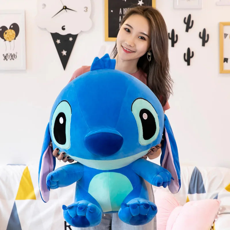 Person holding a large blue plush toy in a room with decorative items on the wall.