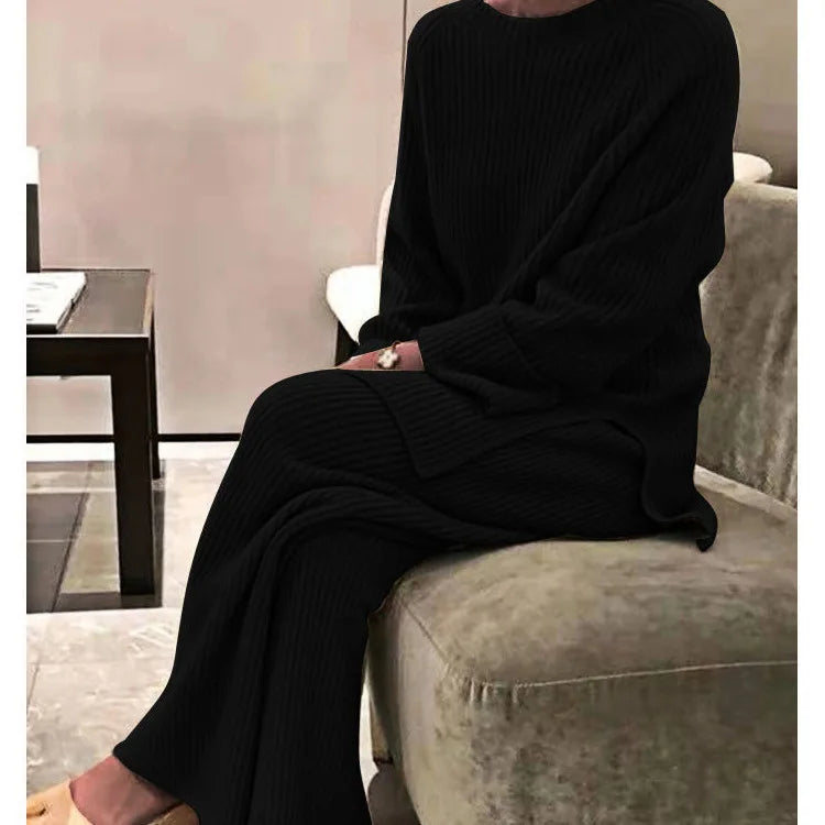 Person wearing a black outfit sitting on a gray sofa in a room with a pink wall.