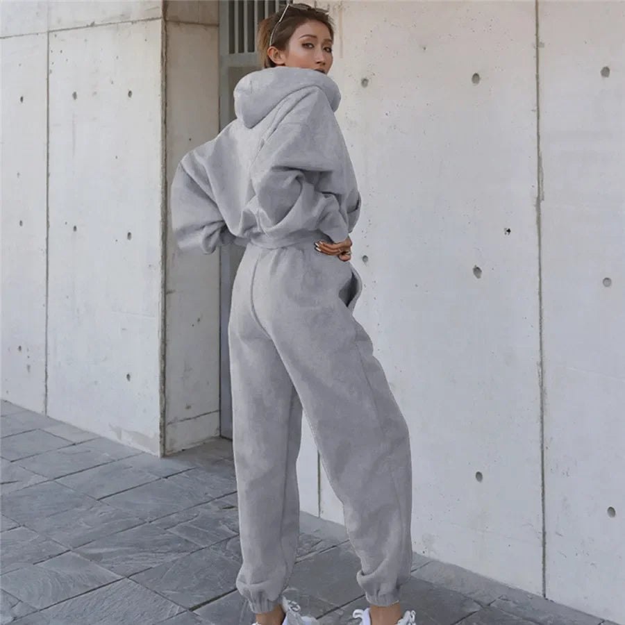 Person wearing a gray tracksuit standing against a light-colored wall.