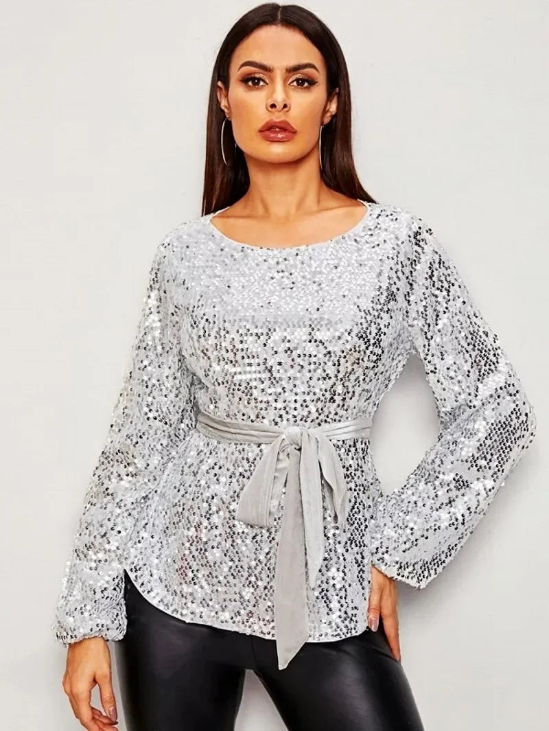 Woman wearing a silver sequin blouse with a tie waist on a white background