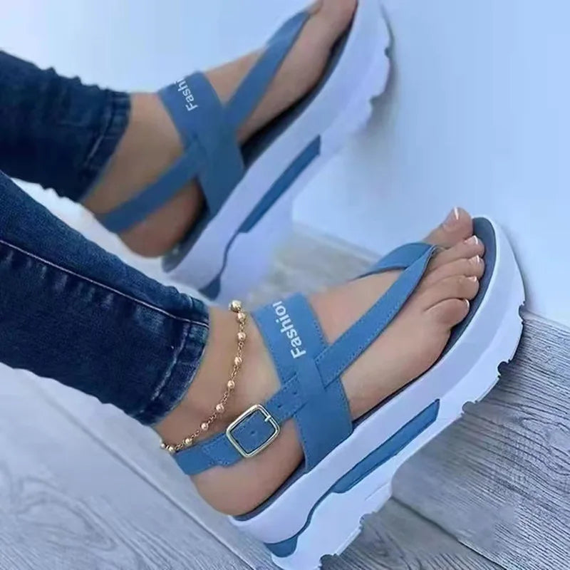 Blue sandals with white soles worn by a person on a light wooden floor.