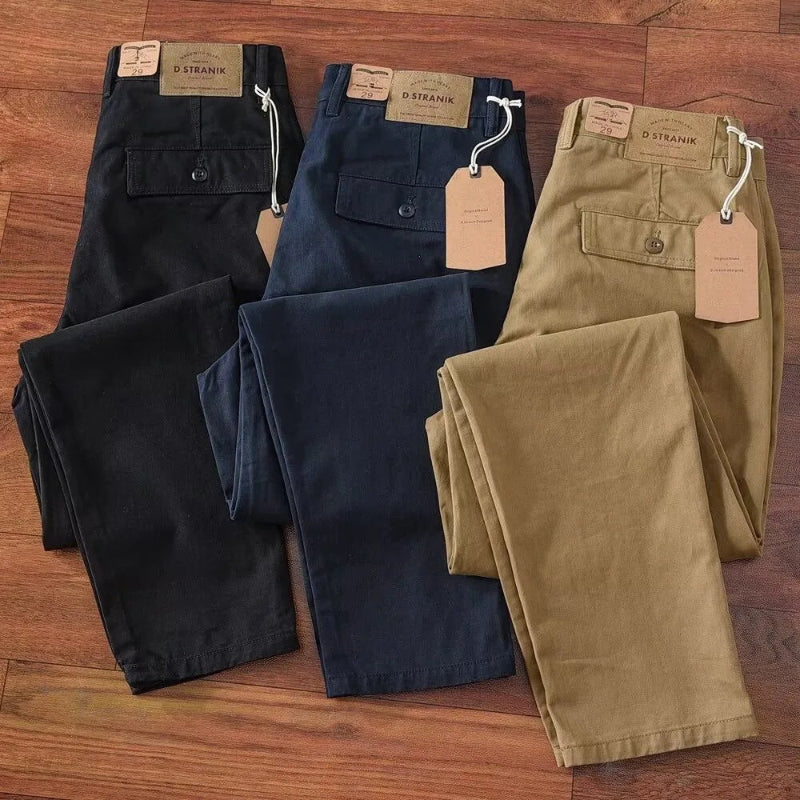 Four pairs of pants in black, navy, and beige on a wooden surface with 'D. Strahm' tags.