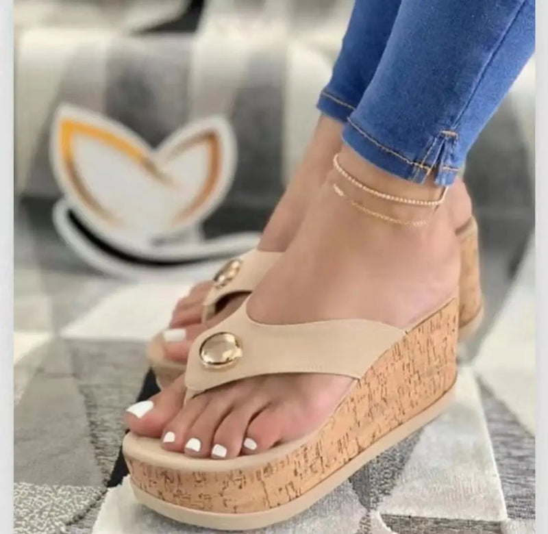 Beige sandals with cork wedge sole worn by a person, with a blurred background.