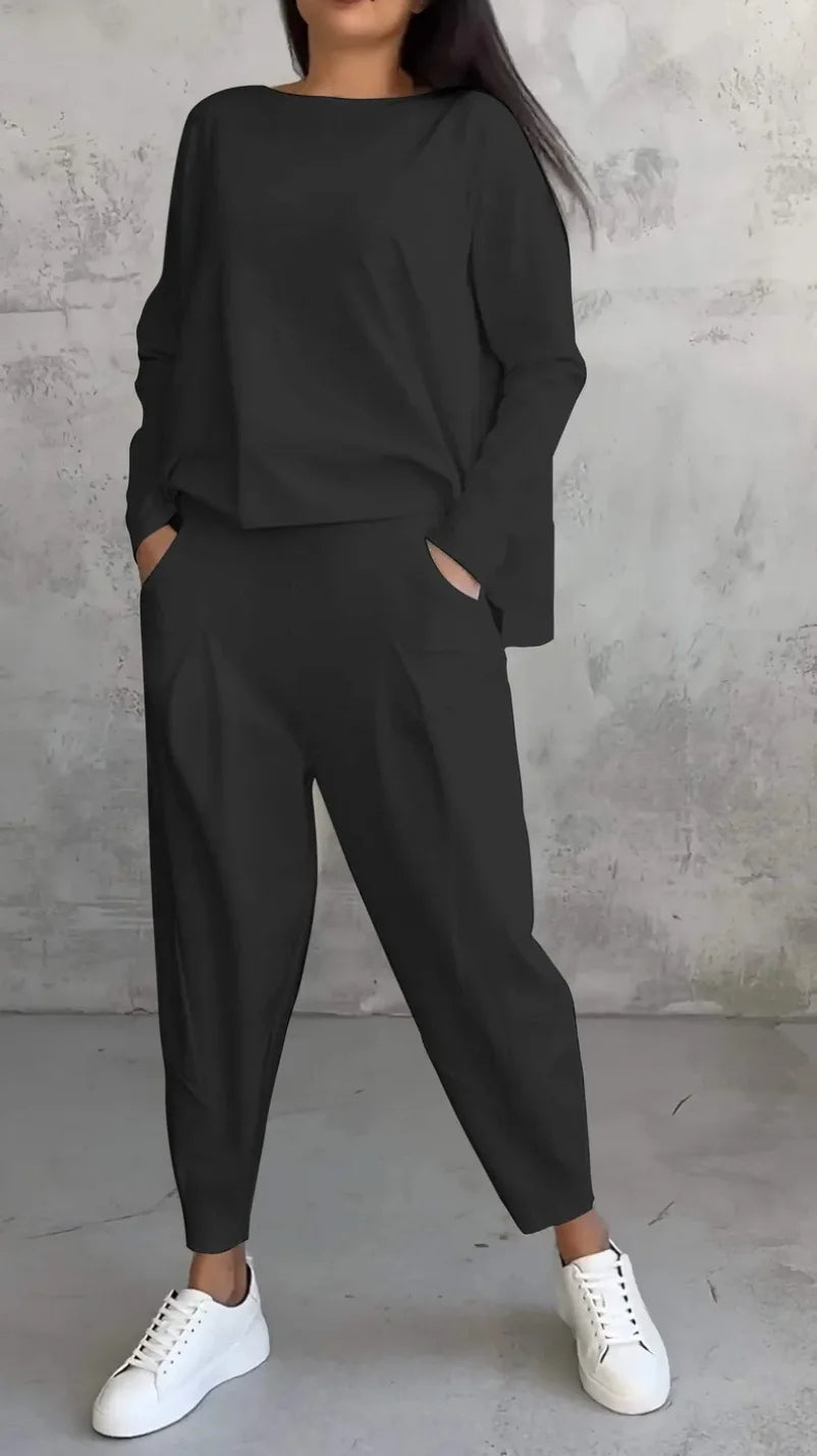Person wearing a black outfit with white sneakers against a gray concrete wall.
