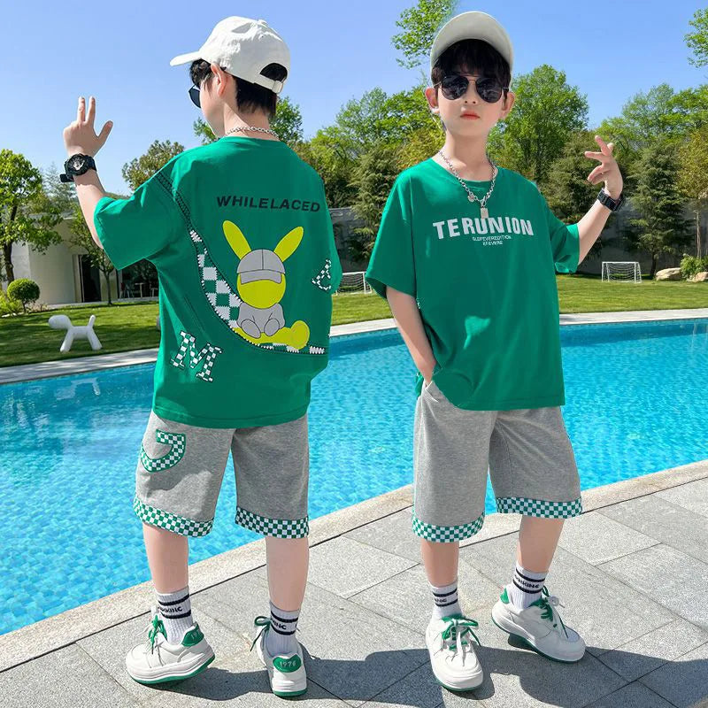 Two children in green t-shirts by a pool with trees in the background