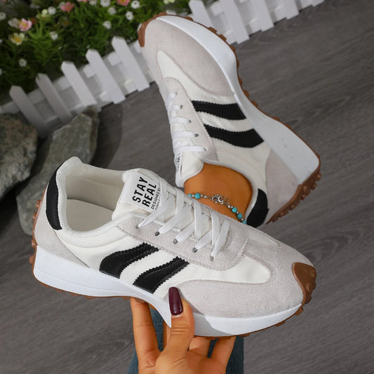 White sneakers with black stripes held by a hand against a blurred outdoor background