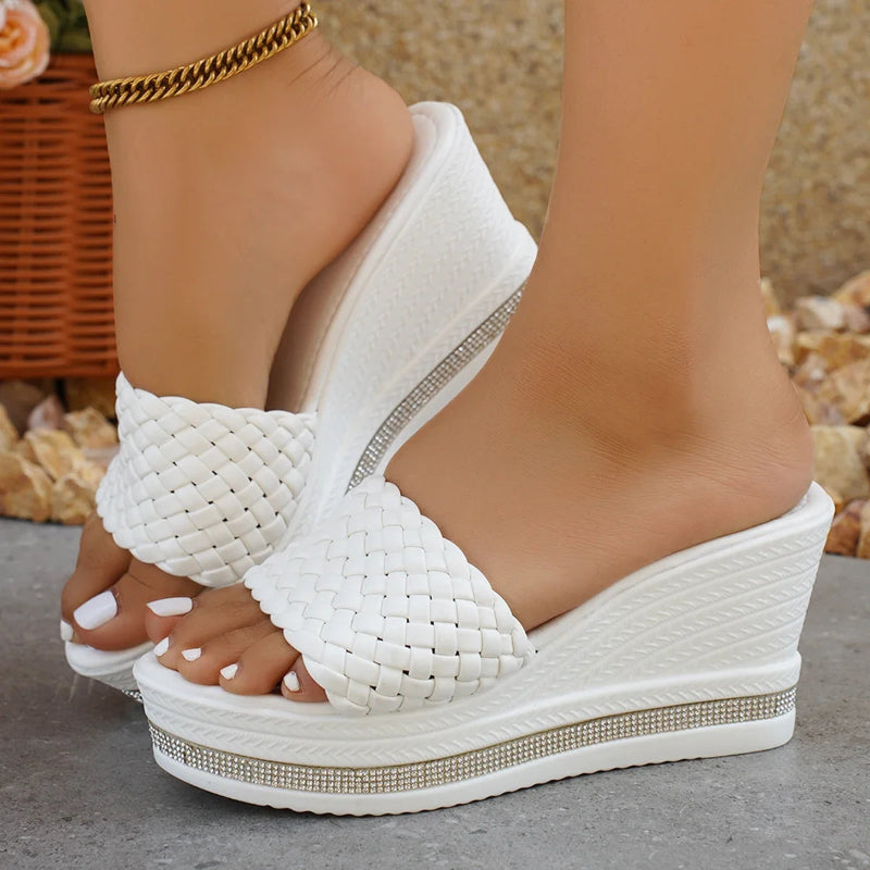White woven wedge sandals with rhinestone details worn by a person.