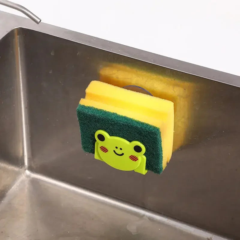 Yellow sponge with a green holder featuring a frog design in a stainless steel sink.