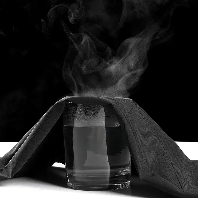 Clear glass with steam rising from it, draped with a black cloth on a dark background