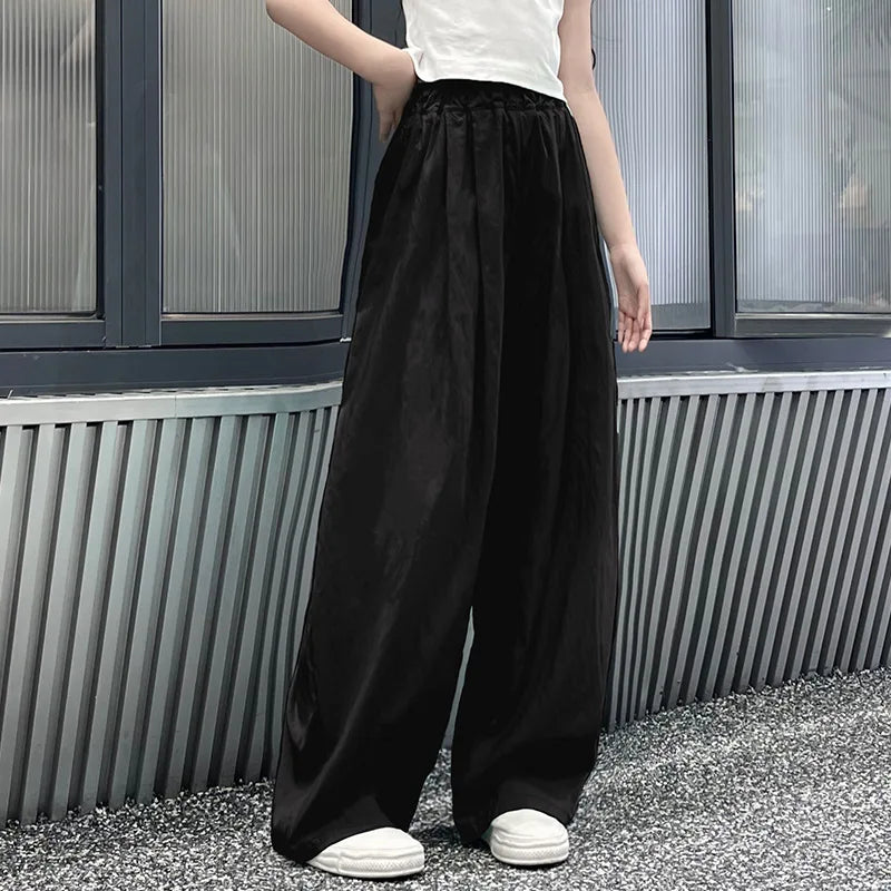 Person wearing black wide-leg pants and white shoes standing against a metallic wall.