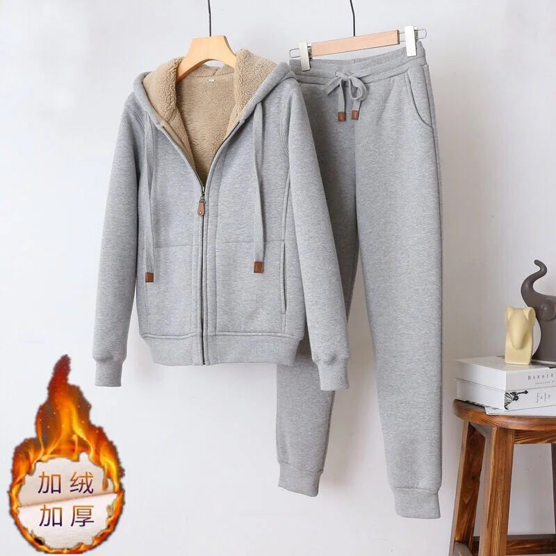 Gray tracksuit with fur-lined hood on hangers against a white wall.