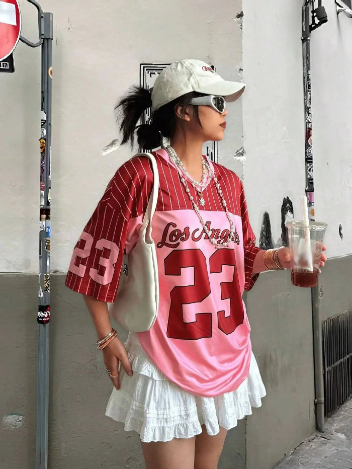 A person wearing a white V-neck T-shirt with the number 23 printed in black, paired with a white skirt, white hat, and holding a drink.