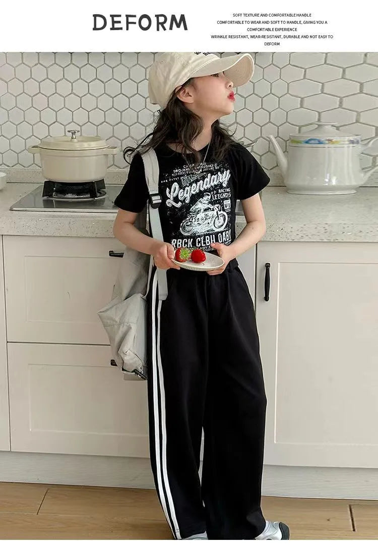 Person wearing a black t-shirt with graphic design and black pants with white stripes in a kitchen.